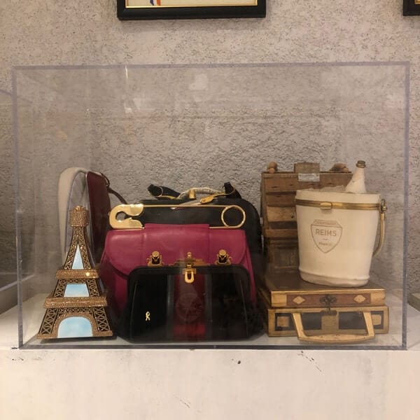 A display from the PURSEonality exhibition featuring a pink safety pin, smaller black bag and a ornament of the Eiffel Tower