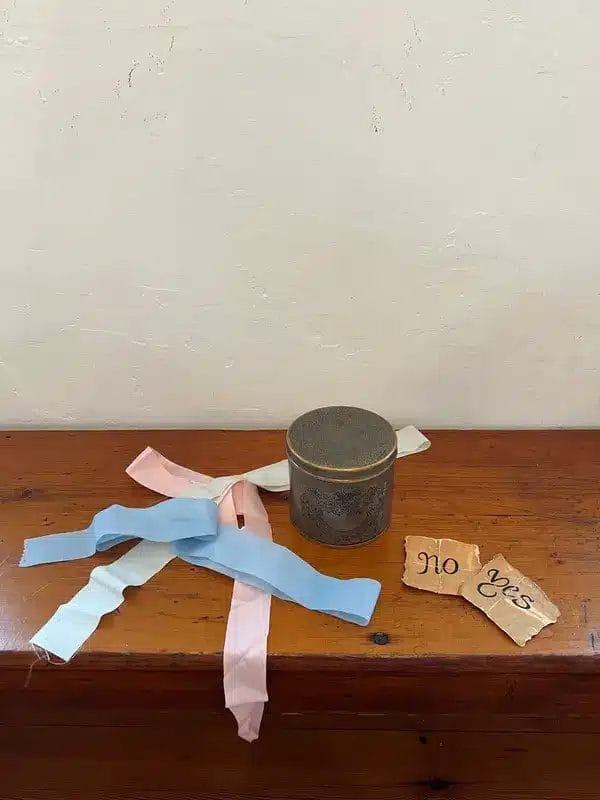 blue, pink, and white ribbons next to a metal jar and two pieces of paper that read "yes" and "no"